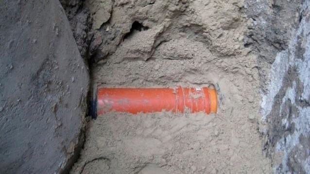 Orange rør begravet i sand i en byggeplads, omringet af jord og sten.