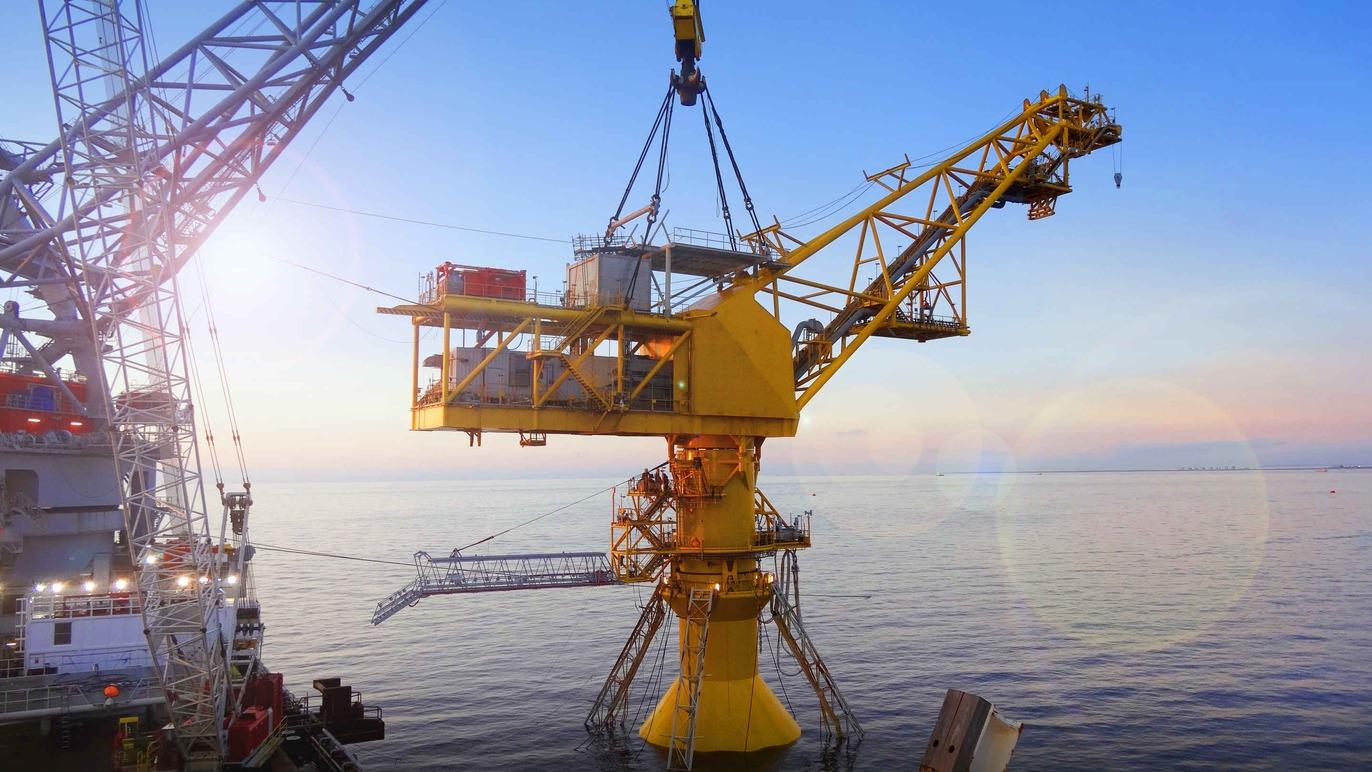 En gul offshore olieplatform med kran, der arbejder over havet ved solopgang.