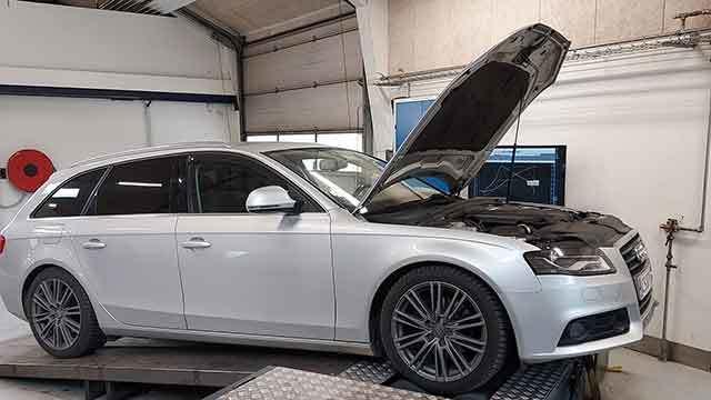 En sølvfarvet Audi stationcar med motorhjelmen åben på et værksted.