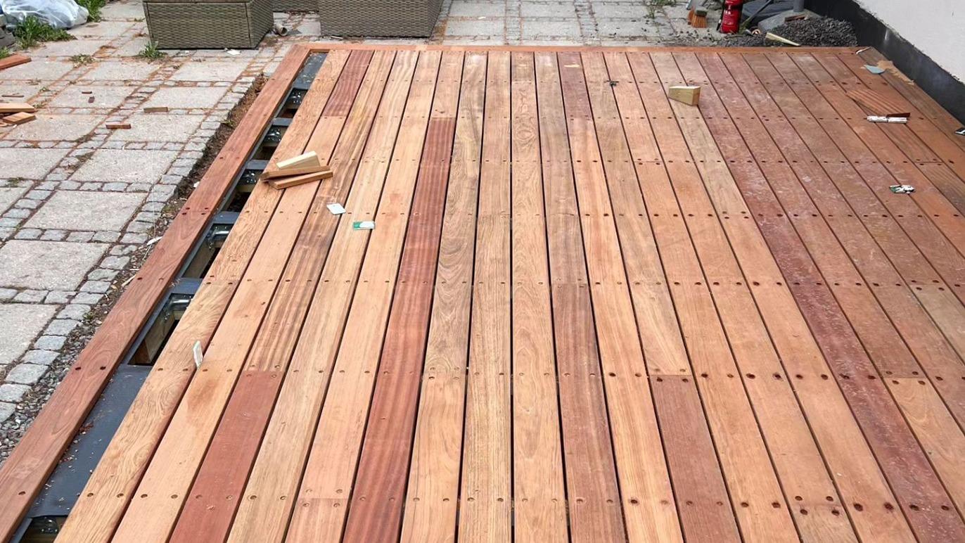 Ny lægning af træterrasse med brune planker på en flisebelagt gård.