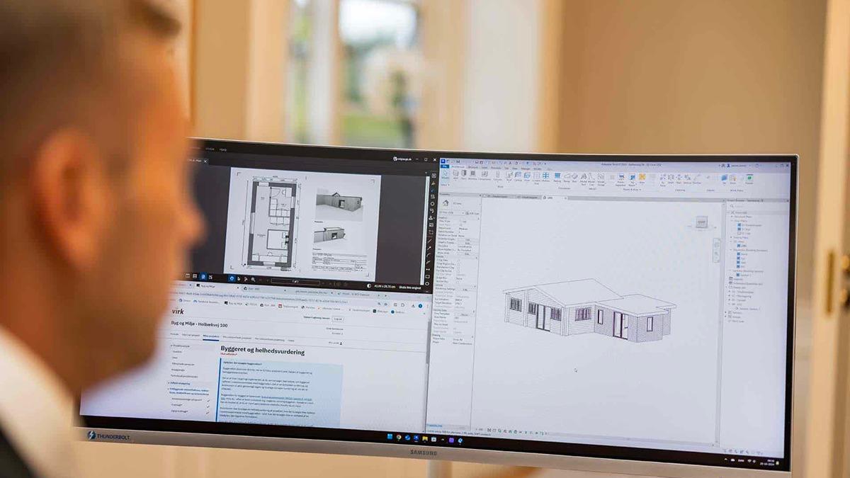 En person sidder foran en computer med skærme, der viser bygningstegninger og 3D-modeller.