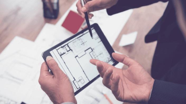En person holder en tablet med en bygningstegning, mens en anden person peger på skærmen.