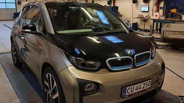 En BMW i3 elbil parkeret i en garage med en sort og sølvfarvet overflade.