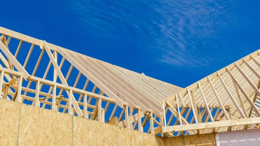 Tagkonstruktion af træ med blå himmel i baggrunden, der viser et hus under opbygning.