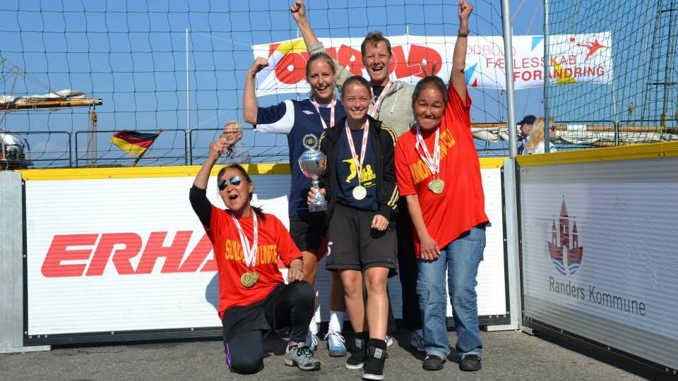 Gruppe af glade vindere med medaljer og trofæ ved en sportsbegivenhed, der fejrer deres sejr.