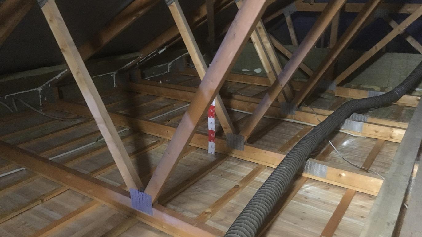 Billede af et loft med synlige træbjælker og en ventilationsslange på gulvet.