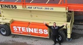 En mand står foran en stor JLG lift med teksten "STEINESS" på siden.