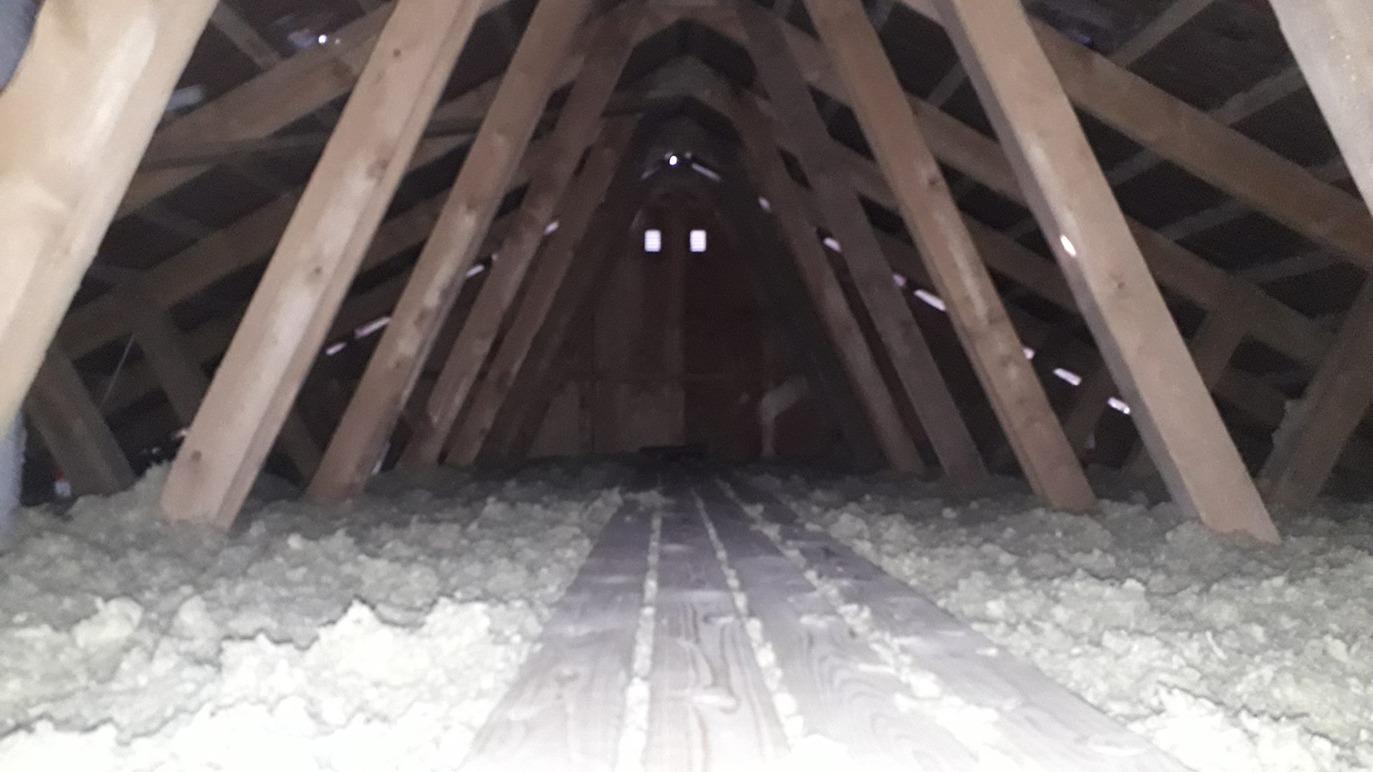 Loft med synlige træbjælker og isolering på gulvet, der skaber en mørk og stille atmosfære.