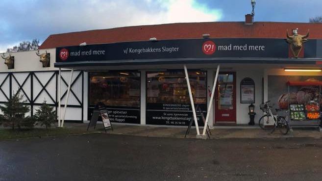 En butik med navnet "mad med mere" med store vinduer og en cykel parkeret foran.