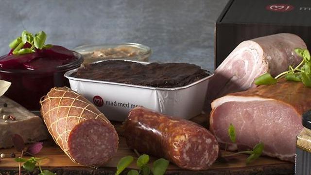 Lækre kødprodukter præsenteret på et skærebræt med tilbehør som syltetøj og sennep.