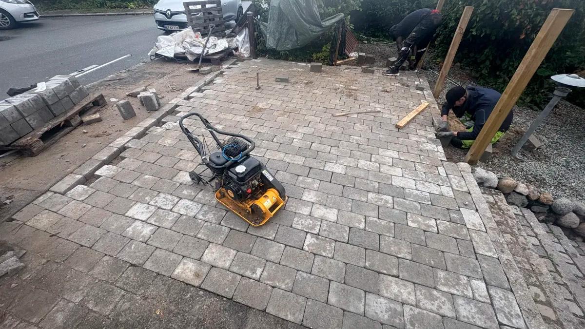 En arbejder bruger en pladevibrator på en nyanlagt stenbelægning ved en byggeplads.