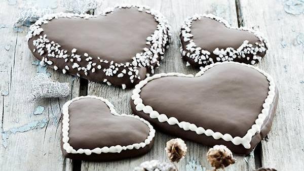 Fire chokoladehjerter med pynt af perlesukker og flødeskum på en træoverflade.