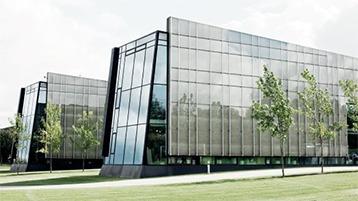 Moderne kontorbygninger med glasfacader og grønne træer i forgrunden.