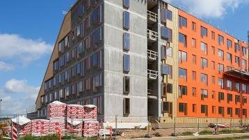 Nybygget lejlighedsbygning med orange og grå facade, byggeplads med materialer i forgrunden.