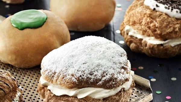 Lækre fastelavnsboller med flødeskum og forskellig pynt på en bageplade.