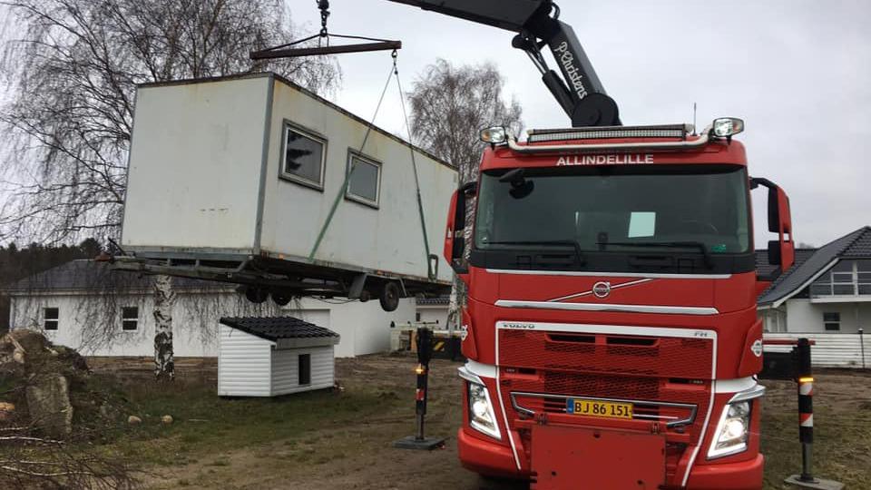 En rød lastbil løfter en hvid container med en kran i et boligområde.