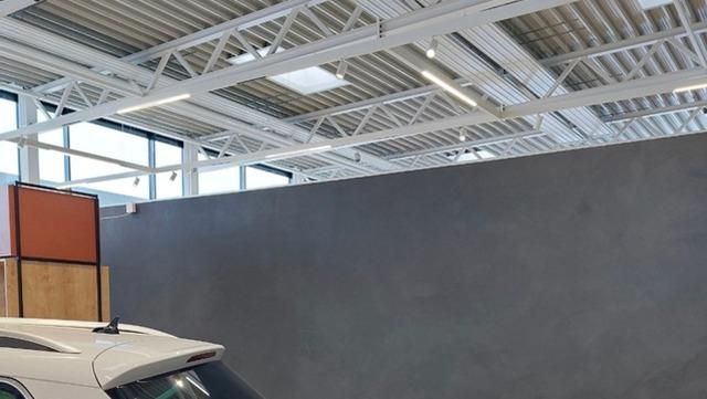 En hvid bil parkeret i en moderne garage med grå vægge og store vinduer.