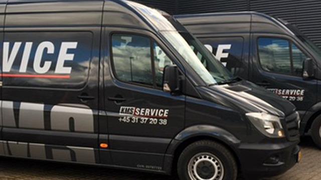 To varevogne med logoet "LMS Service" parkeret ved en bygning.