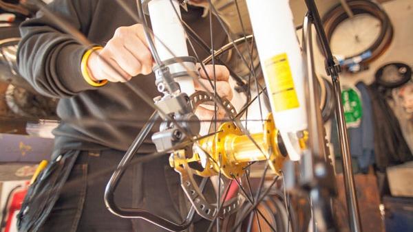 En person reparerer en cykel i et værksted, mens de justerer bremserne og navet på forhjulet.