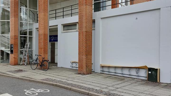 Facade af bygning med mursten, cykel parkeret og tom væg, der venter på udsmykning.