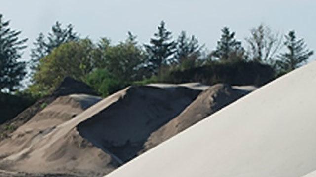Sandbakker og træer i baggrunden under en klar himmel.