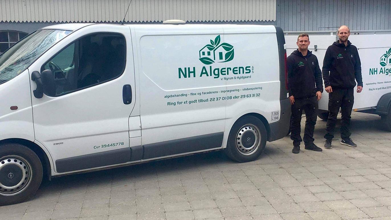 To personer står ved siden af en hvid varevogn med NH Algerens logo på siden.