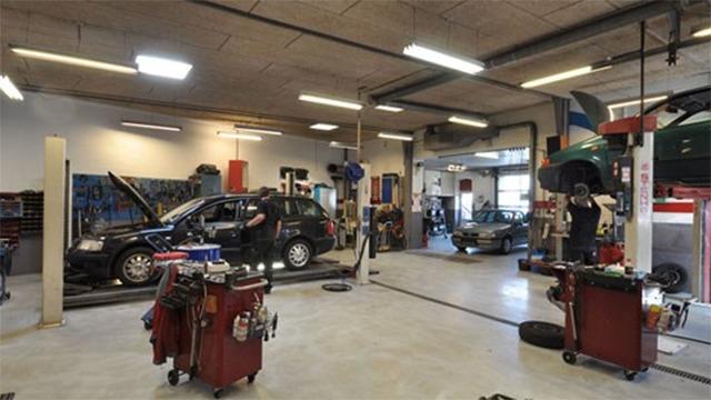 Et moderne autoværksted med flere biler, værktøj og arbejdsstationer til reparation og vedligeholdelse.