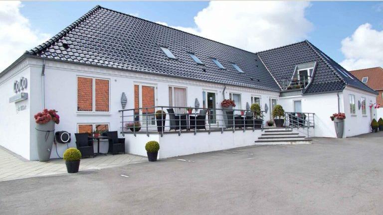 En moderne hvid bygning med sorte tagfliser, terrasse og blomsterkasser foran.