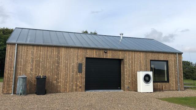 Moderne træhus med metaltag, garageport og vaskemaskine foran, beliggende på en grusvej.