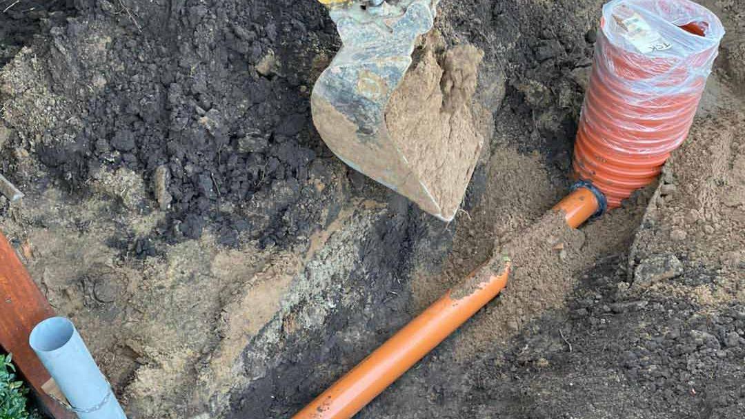 Gravested med orange rør og en spade, der ligger på jorden, omgivet af jord og sten.