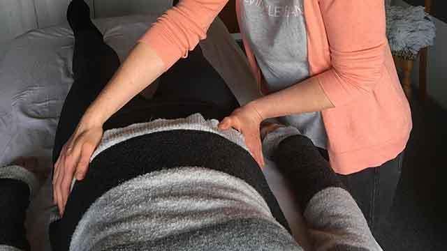 En massør giver en rygmassage til en klient, der ligger på en behandlingsbriks.