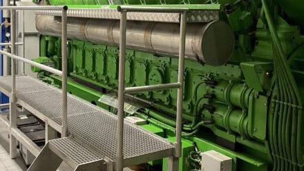 Stor grøn motor med metaltrapper i en industriel bygning.