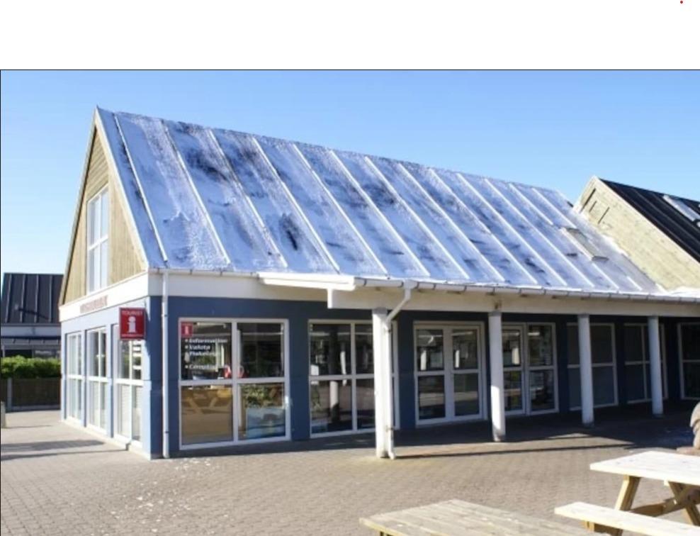 Moderne bygning med skråtag og store vinduer, beliggende i et åbent område med bænke foran.