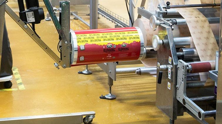 Maskine til emballering af produkter med rød beholder og etiketter i en produktionshal.