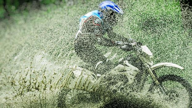 En motocrossrytter kører gennem mudder og sprøjtende vand i en skov.