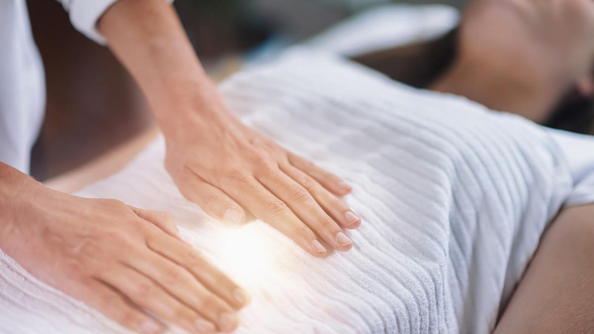 En behandler udfører healing på en person, der ligger på en behandlingsbriks med en hvid dyne.
