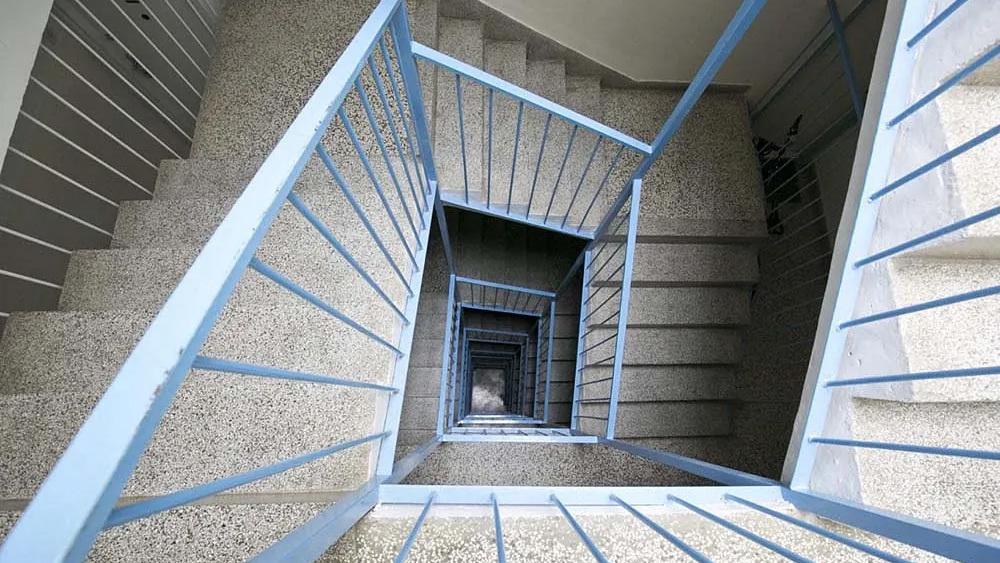 Billede af en spiraltrappe med grå vægge og blå rækværk, der fører nedad i en bygning.