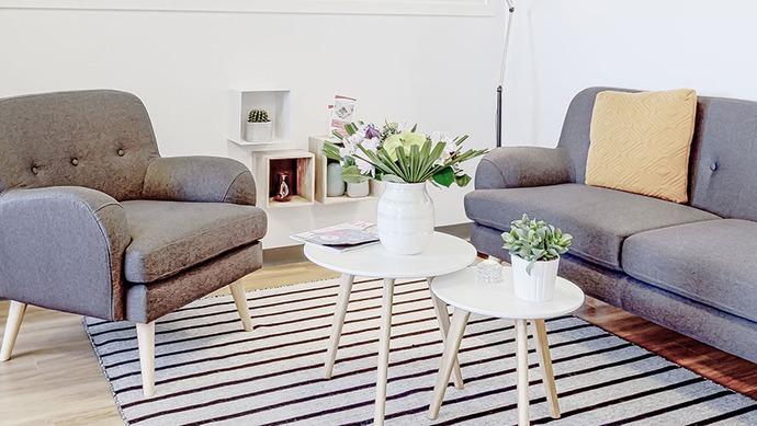 Moderne stue med grå sofa, to lænestole, små borde og blomster i en vase på et stribet tæppe.