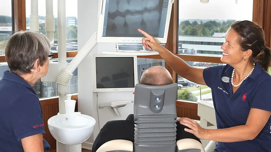 To tandlæger, der viser røntgenbilleder til en patient i en moderne tandklinik.
