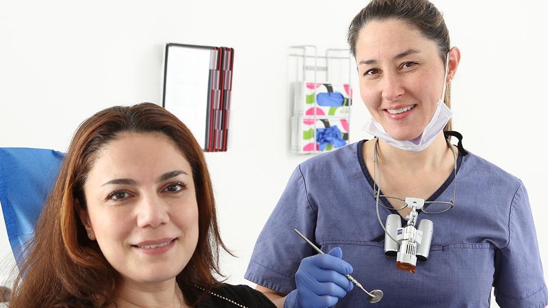 To kvinder i tandlægeklinik, en tandlæge med instrumenter og en patient, der smiler.