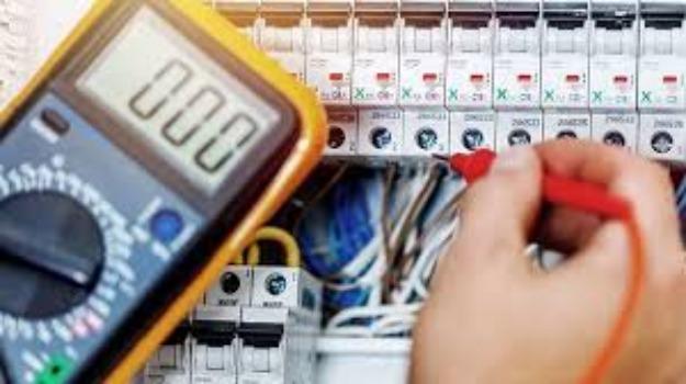 En elektriker bruger et multimeter til at måle spænding på en elektrisk tavle med ledninger og sikringer.