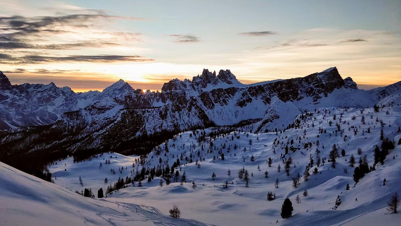 En snedækket bjerglandskab i Dolomitterne ved solnedgang med sneklædte skråninger og klippeformationer.