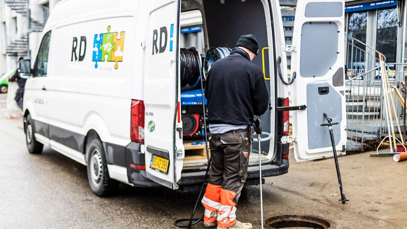 En håndværker står ved en servicevogn og arbejder med udstyr ved en brønd.