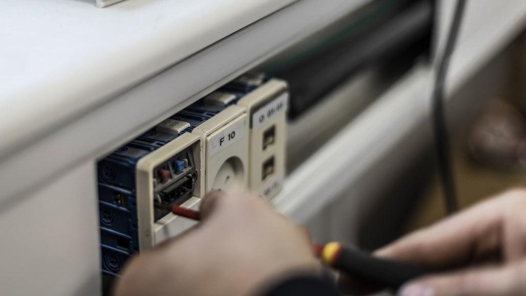 En hånd arbejder med elektriske ledninger i en stikkontakt, mens der bruges værktøj til installation.