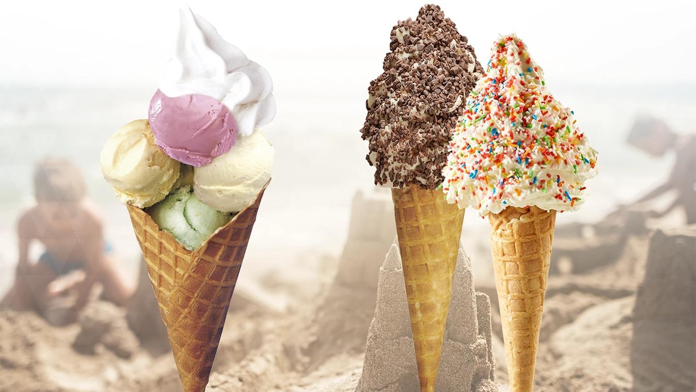 Tre isvafler med forskellige smagsvarianter, herunder chokolade, vanilje og jordbær, på en strand.