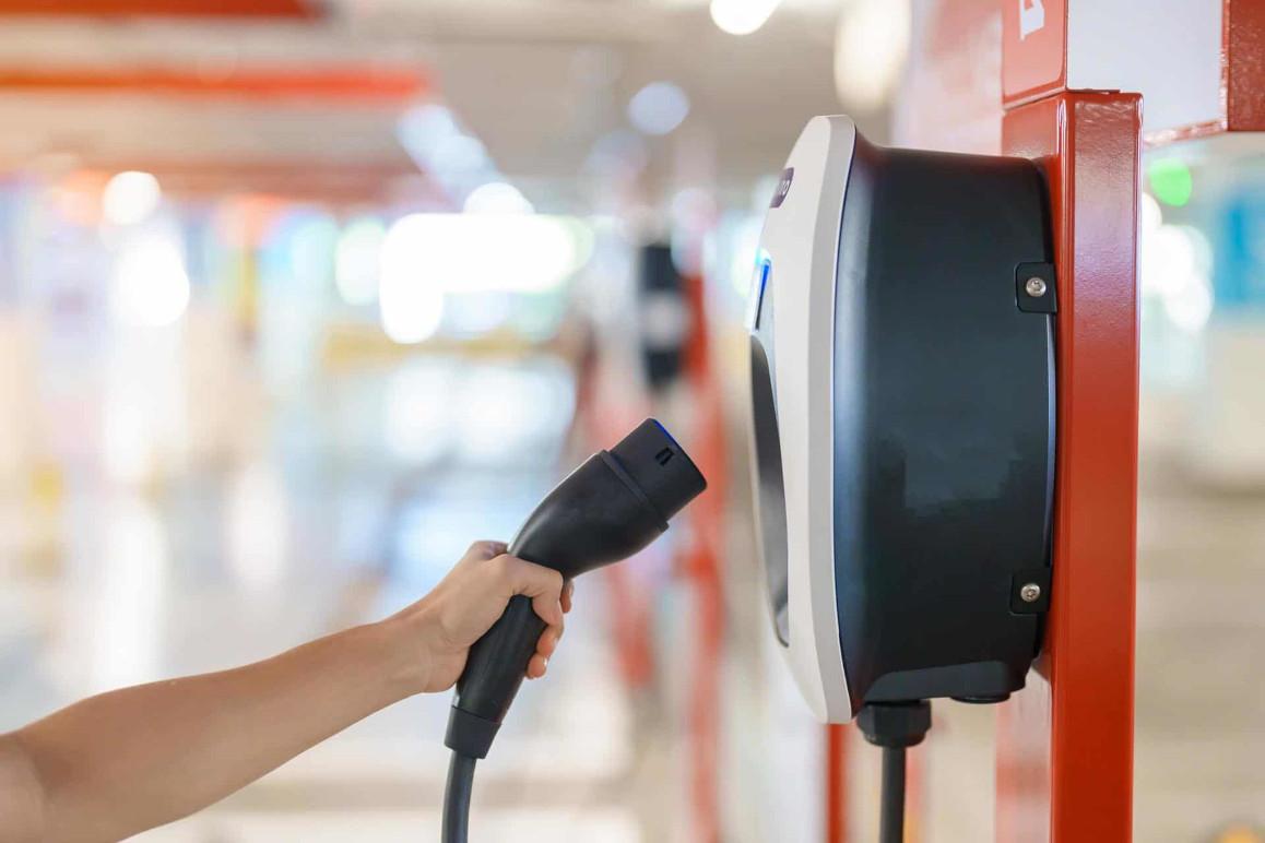 En person tilslutter en ladekabel til en elbil-lader i et parkeringshus.