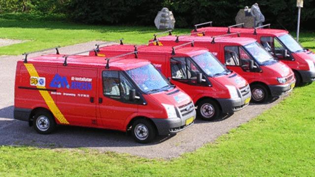 Fem røde varevogne parkeret i en række på en græsplæne, med logoer og tagbøjler synlige.