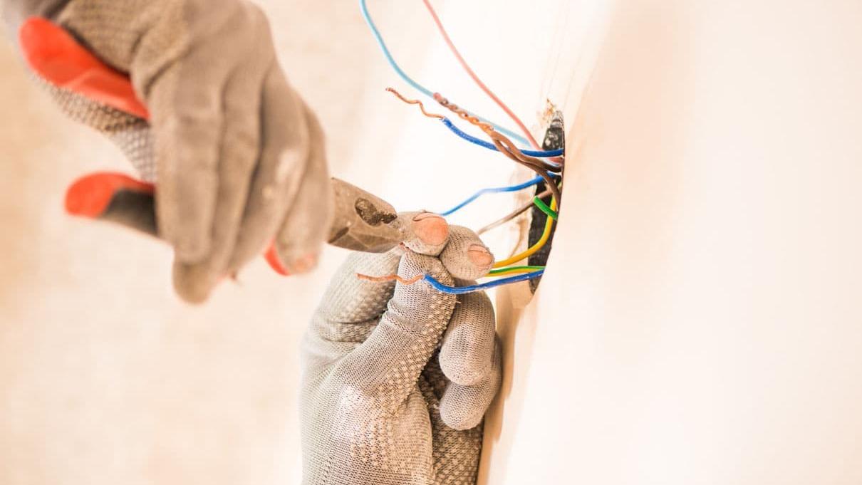 En elektriker arbejder med ledninger og værktøj, mens han installerer elektriske forbindelser på en væg.