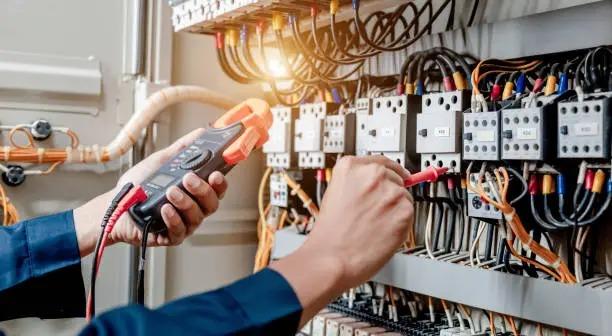 En elektriker bruger et multimeter til at teste elektriske forbindelser i et kontrolpanel.