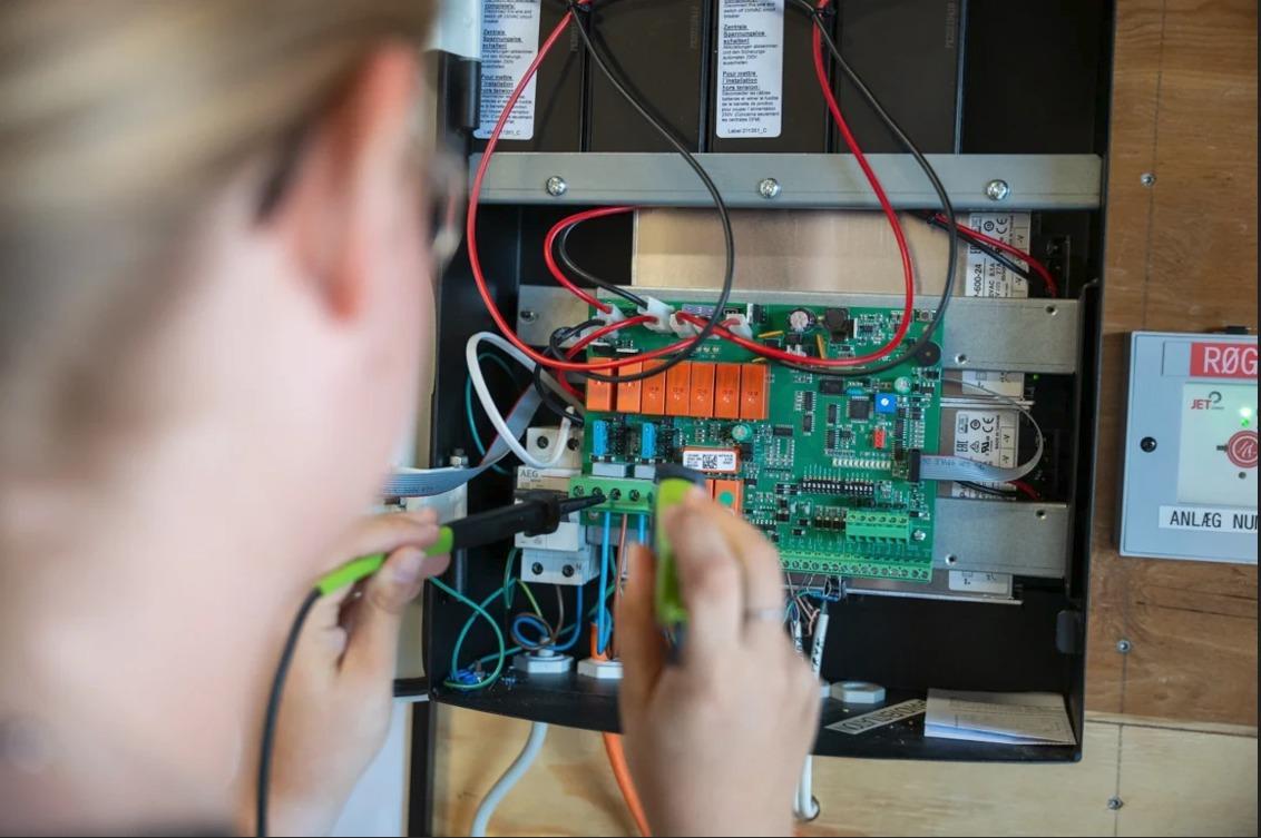 En person arbejder med elektriske kredsløb på en kontroltavle med ledninger og komponenter.